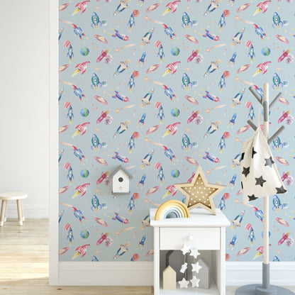 Wallpaper with space-themed design featuring rockets, planets, and stars on a light blue background. Below the wallpaper, there is a white shelf with decorative items.
