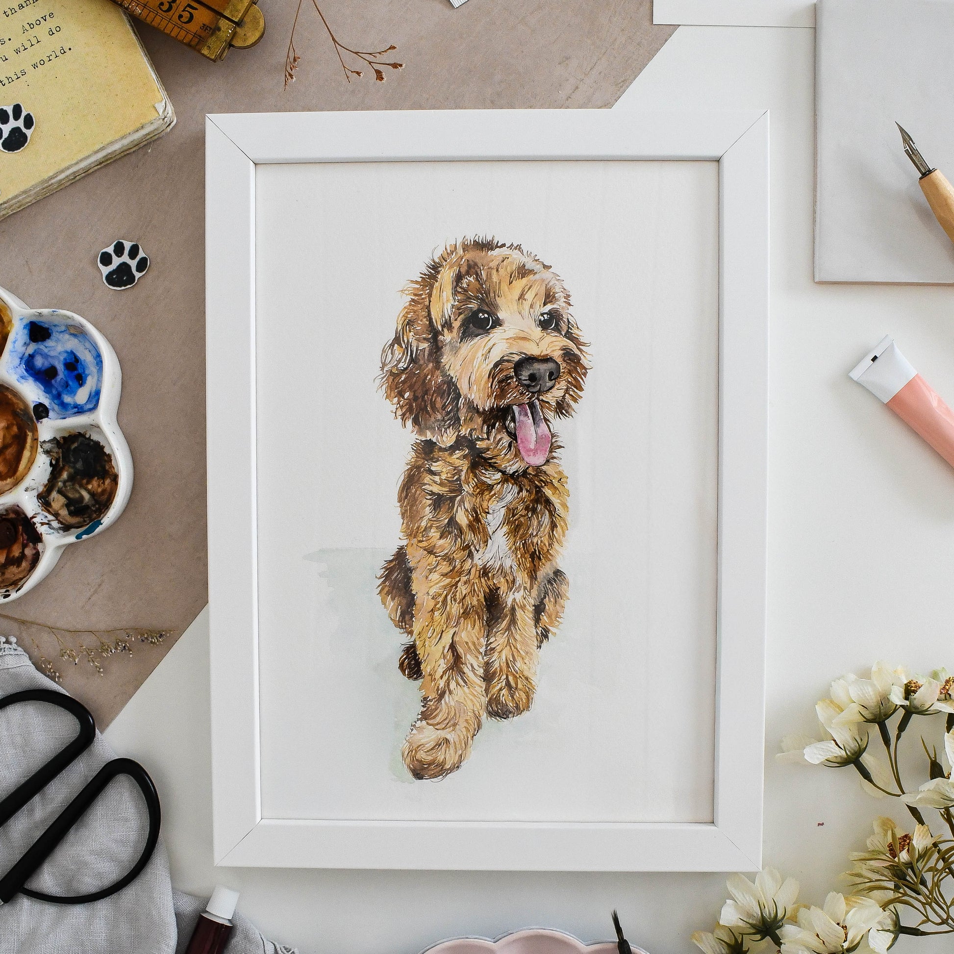 Framed artwork of a hand-painted cockapoo on a table with art supplies