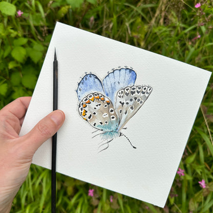 Hand holding a drawing of a butterfly on a white sheet with a natural background