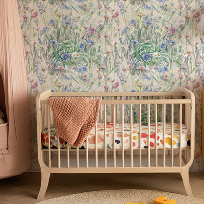 Beige crib with colorful bedding against a floral wallpapered wall