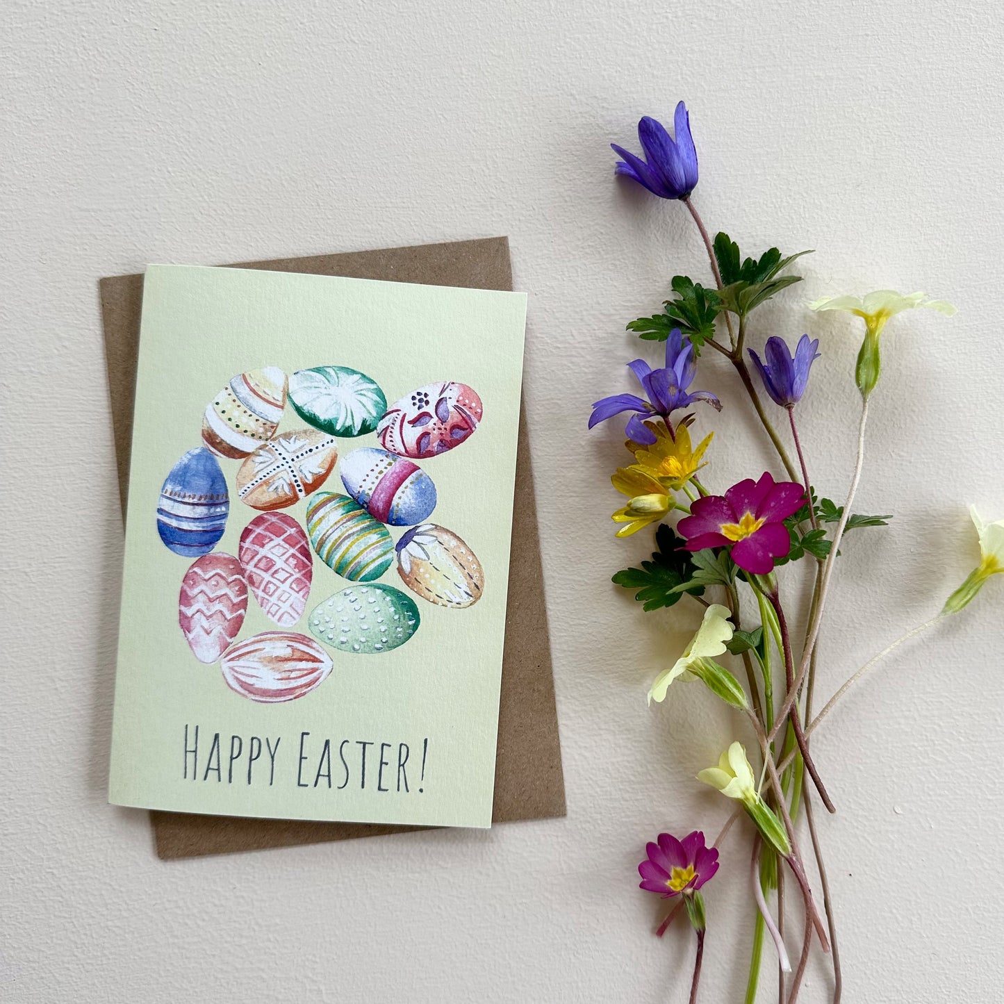 Easter card with colorful eggs and 'Happy Easter!' text, accompanied by spring flowers on a light background.