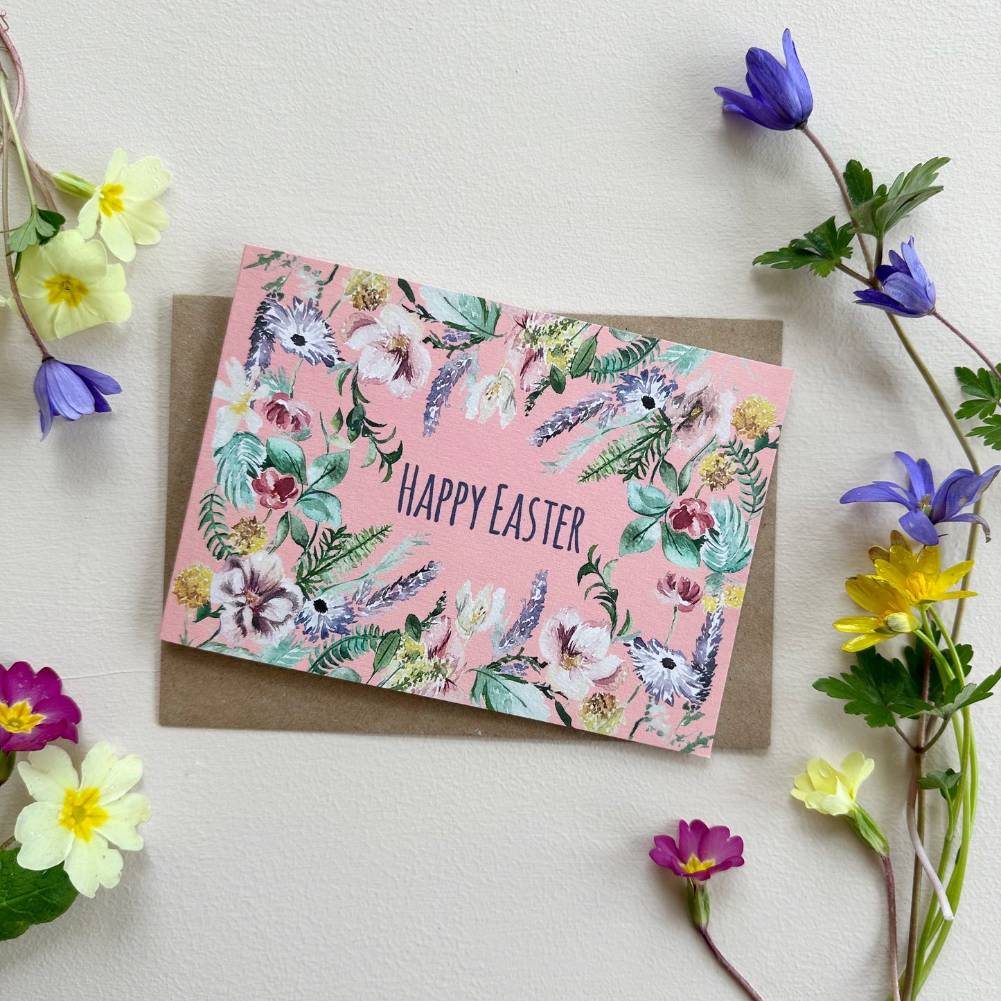 Floral Easter card with 'Happy Easter' text on a pink background, card surrounded by flowers.