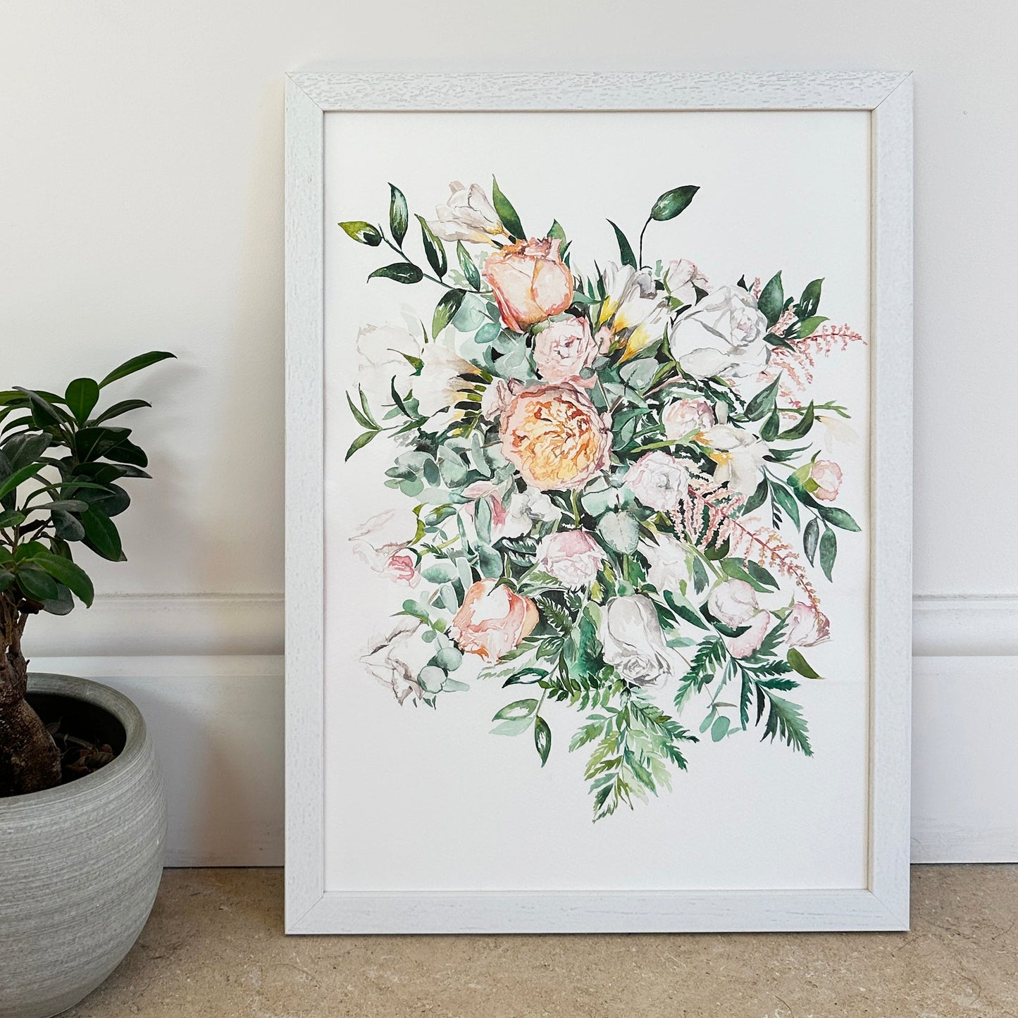 Framed floral artwork on a wall next to a potted plant.